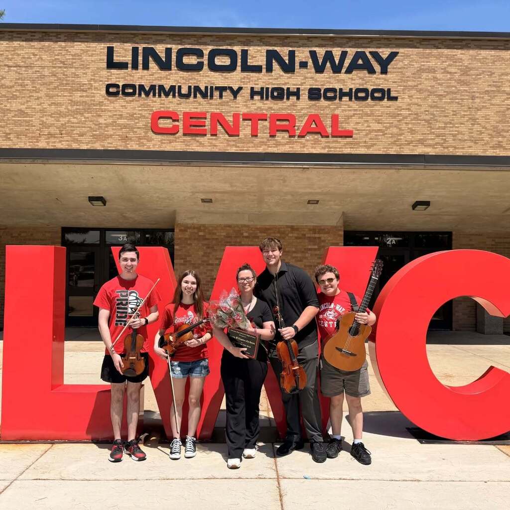 Five individuals stand in front of a large red sign reading "LMC" at Lincoln-Way Community High School Central.