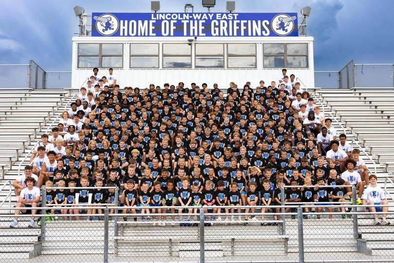 A group of athletes in black jerseys poses for a group photo on bleachers. A sign reads "Home of the Griffins".