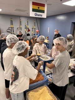 People in a room wearing hairnets, prepare food from large containers.