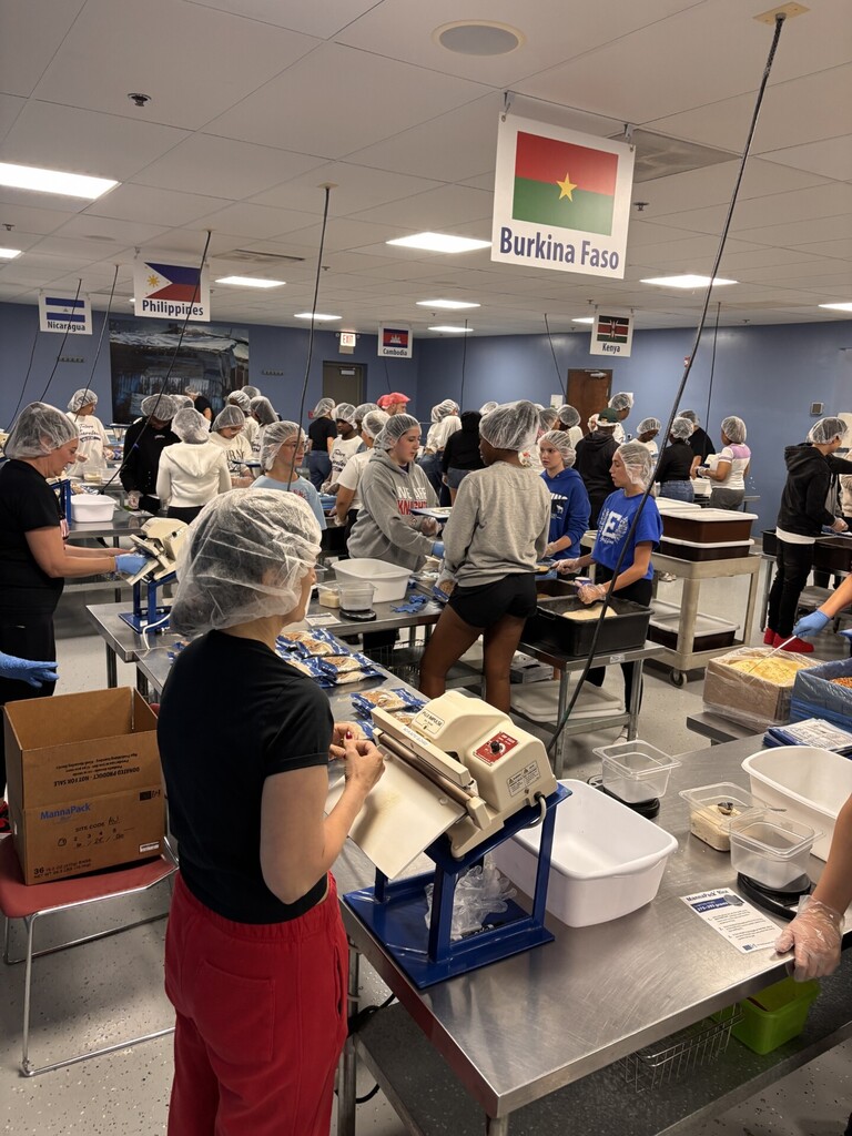 Several people wearing hairnets and gloves work in a kitchen.