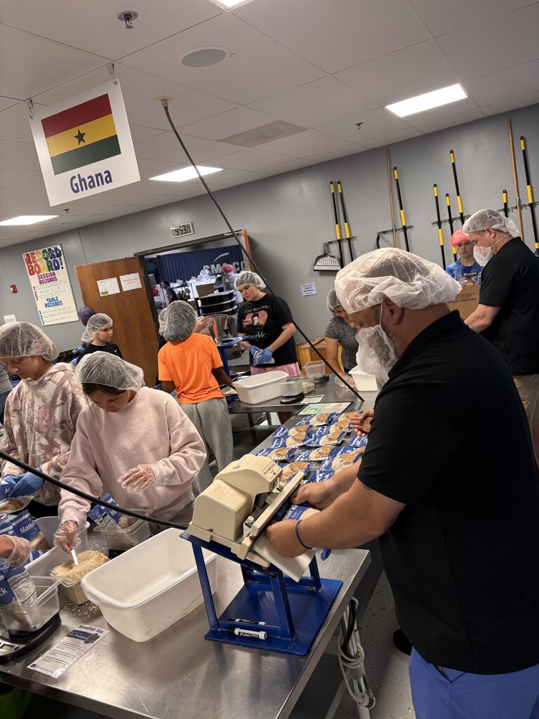 Workers wearing hairnets and face masks prepare food in a kitchen.