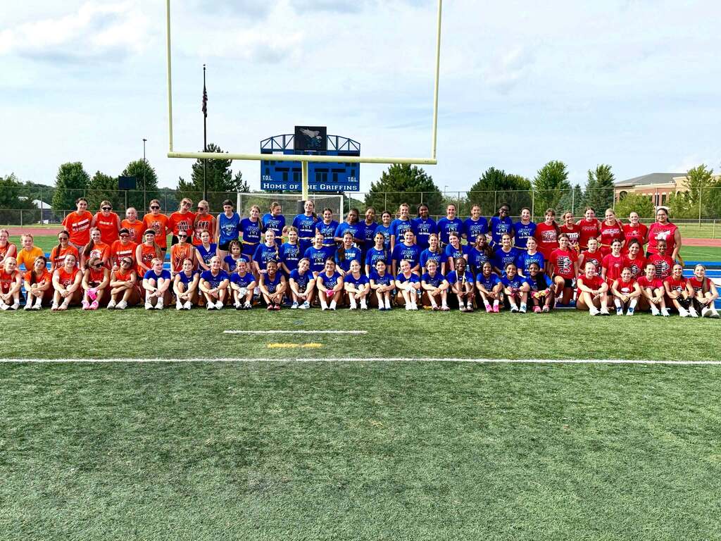 Group of flag football players in orange, blue. and red uniforms, posing for a photo on a field.