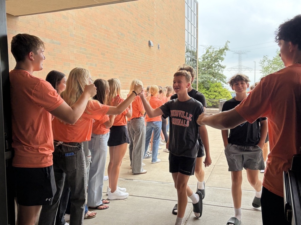 A group of people in orange shirts standing outside a building, some shaking hands and conversing.