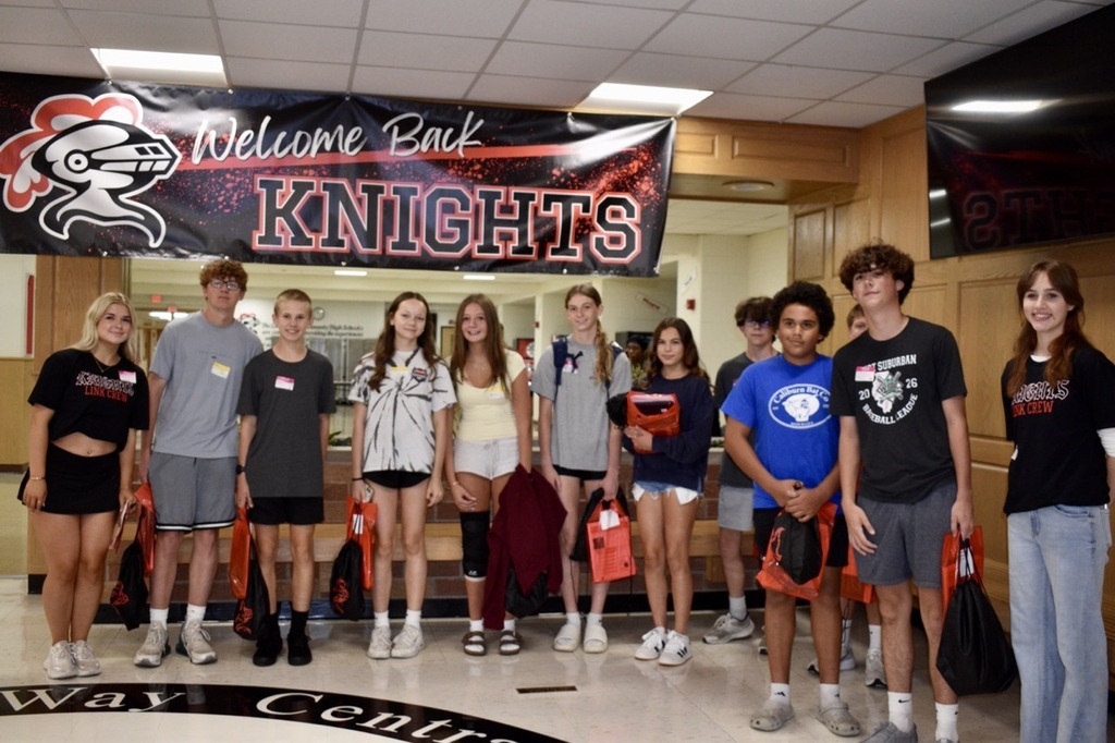 A group of students, wearing varied casual attire, stands in a hallway under a "Welcome Back Knights" banner.