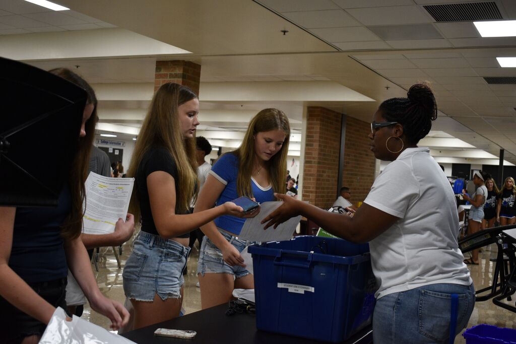 People gather around a table. One holds a blue box. Another holds a white bag.