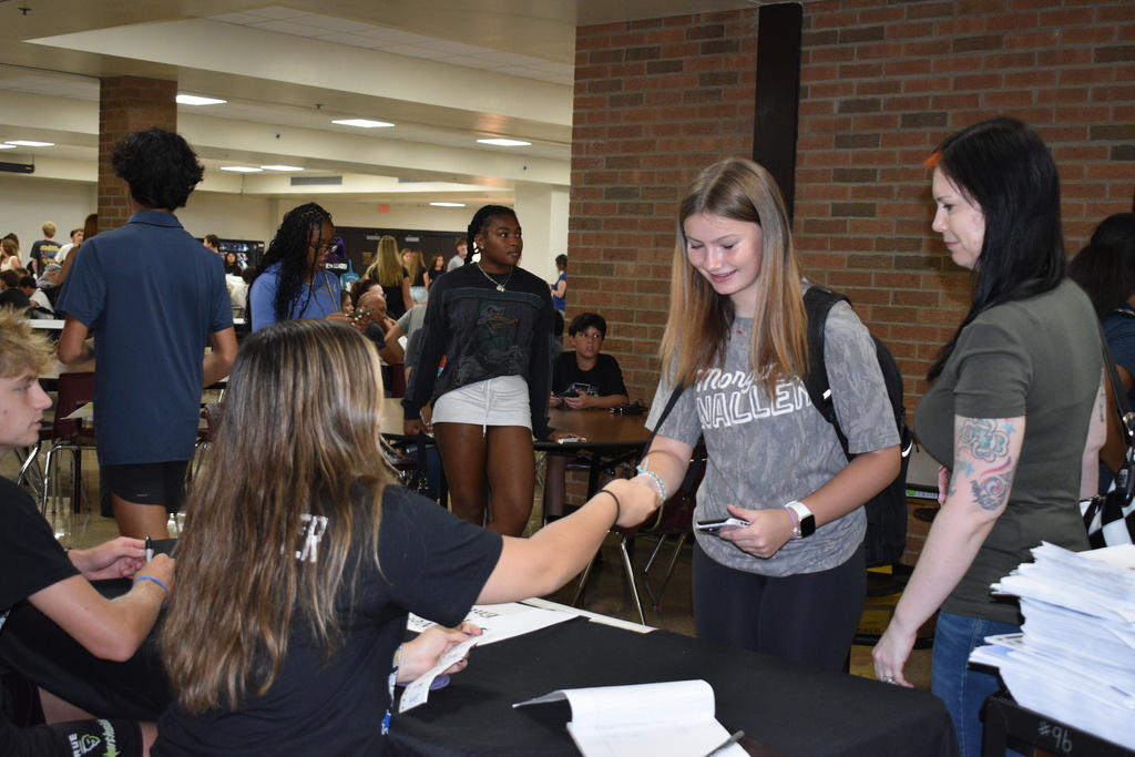 A group of people in a room with brick walls. Two women stand near a table with papers.
