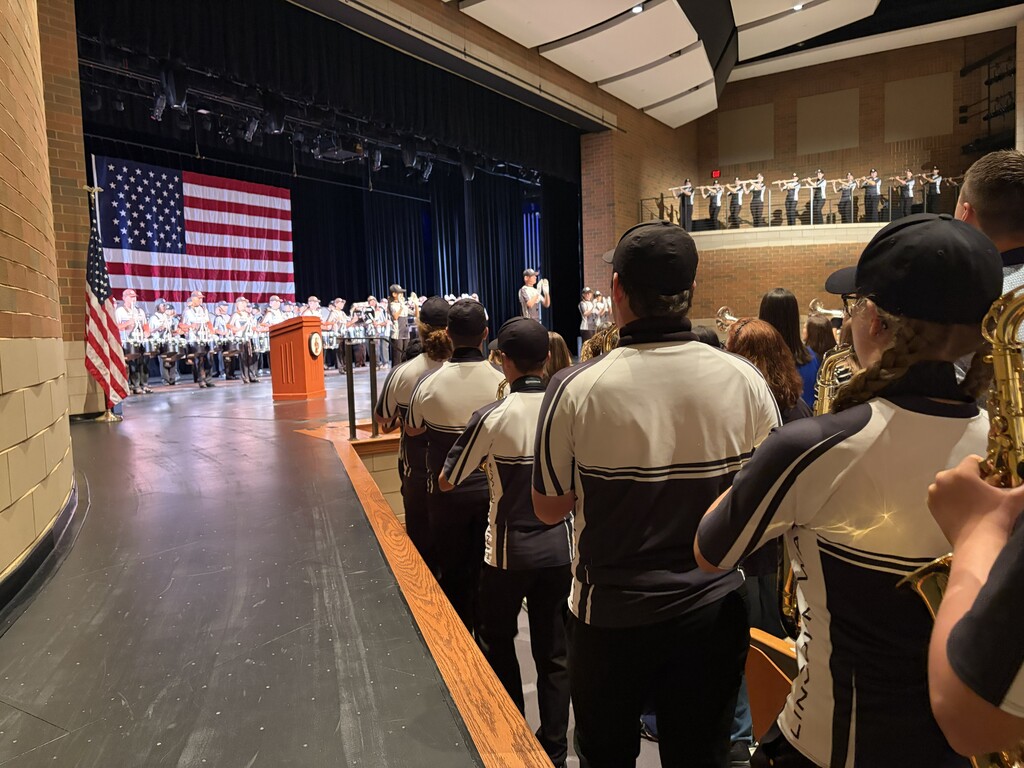 A group of people in matching uniforms stand facing an auditorium stage with an American flag.