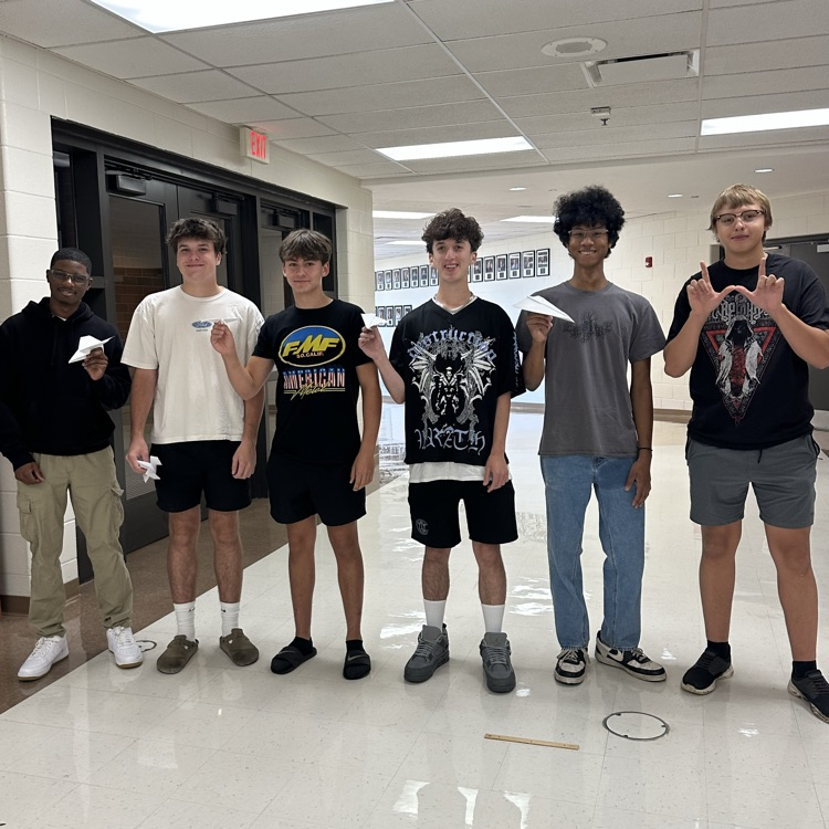students holding paper airplanes in the hallway