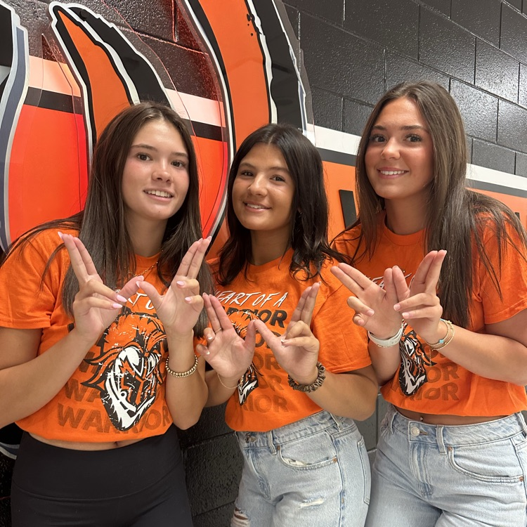 three students wearing orange and holding a W
