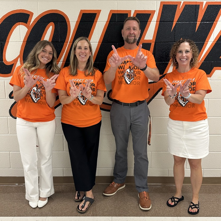 four staff members in hallway holding up Ws with their hands