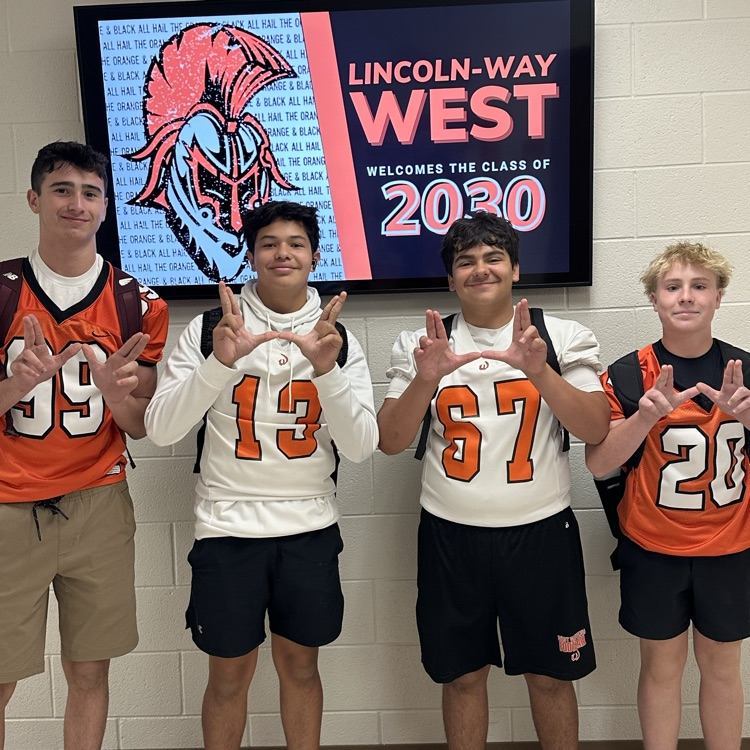 four students in football jerseys holding up Ws with hands
