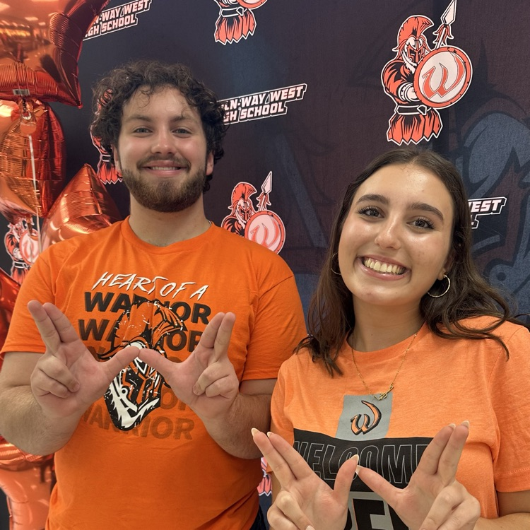 two students in front of school backdrop holding up Ws with hands