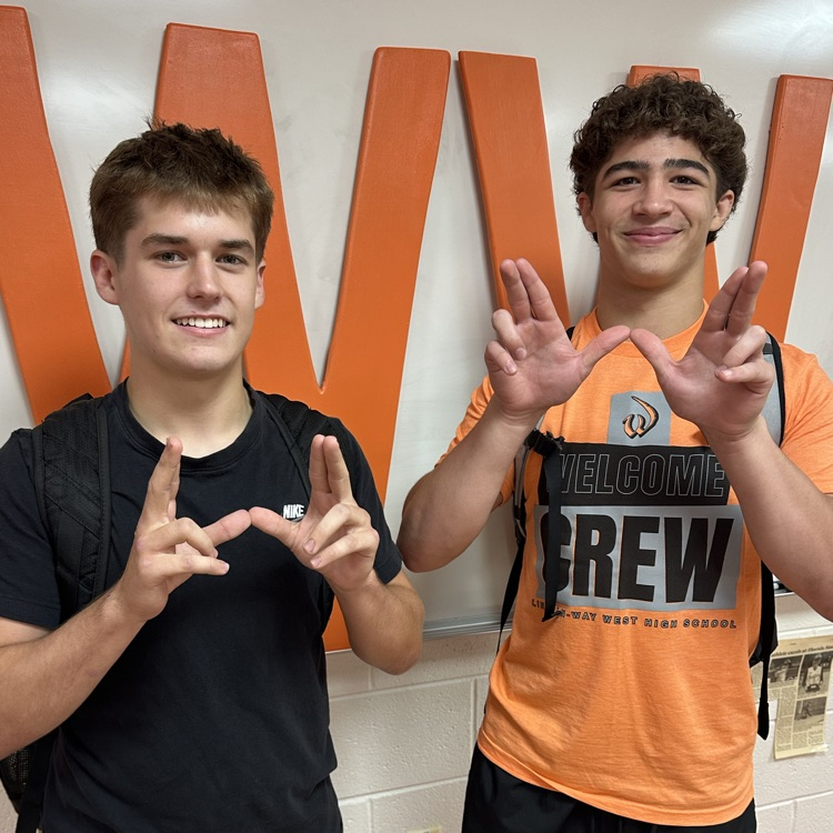 two students in classroom holding up W with hands