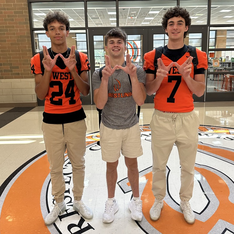 three students standing in front of the library holding Ws