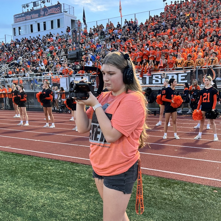 student filming the football game in front of the stands