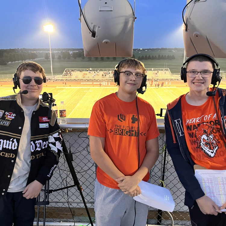three students with headphones on broadcasting football game