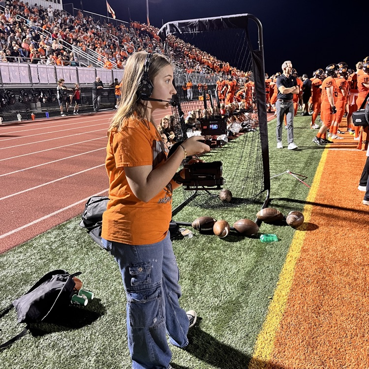 student standing on the sidelines filming football game