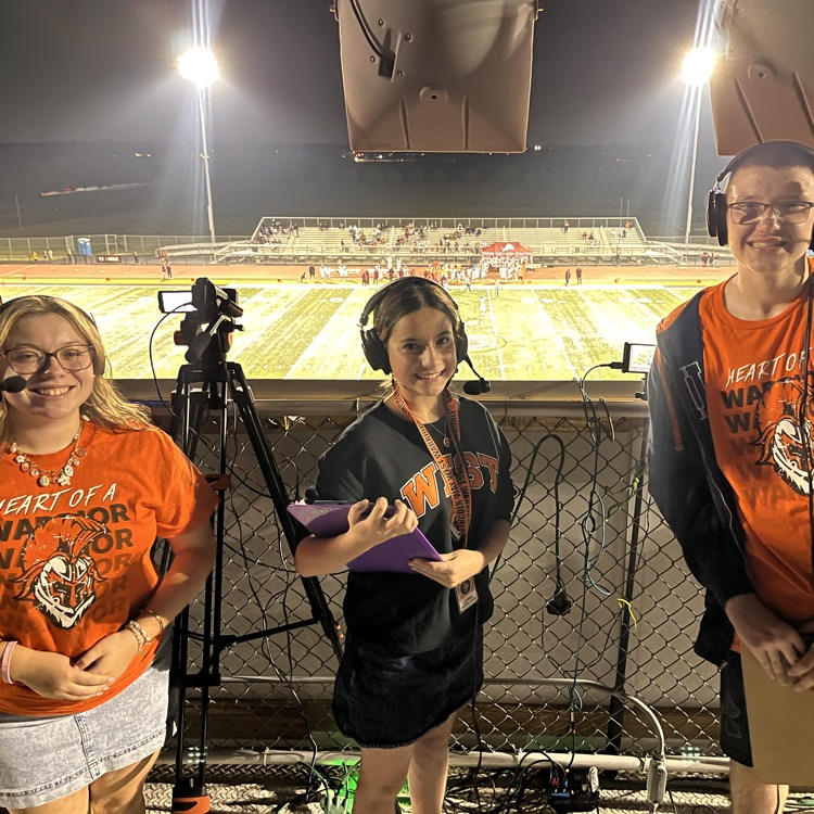 three students with cameras filming the football game from the press box