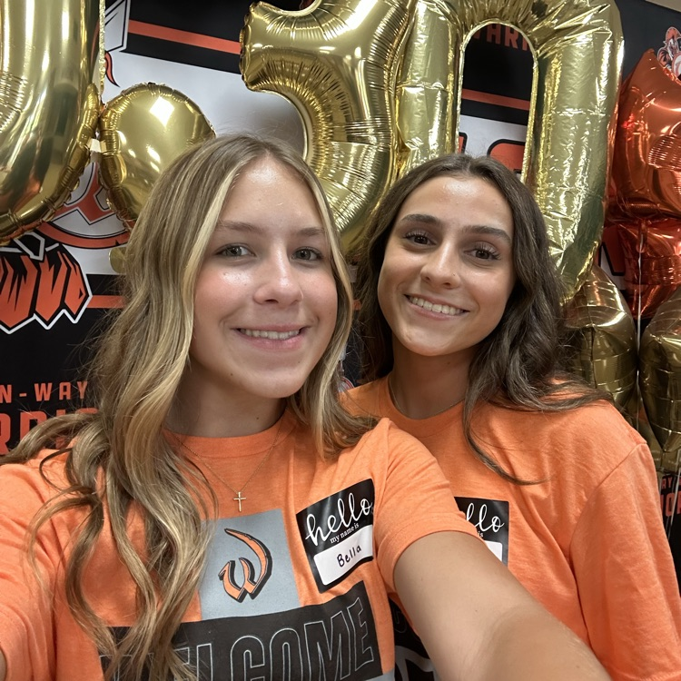 two students taking a selfie in front of school backdrop