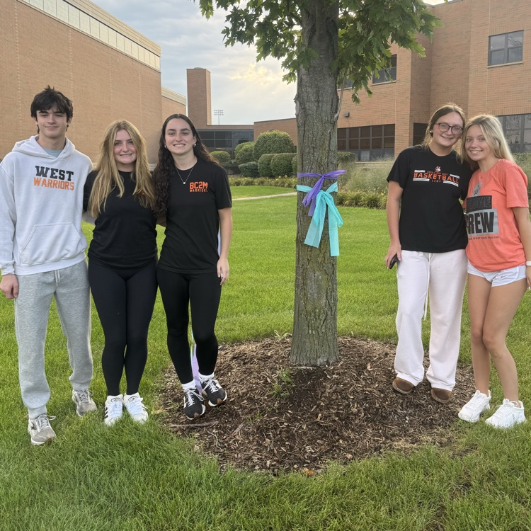 five students posing for a photo in front of tree