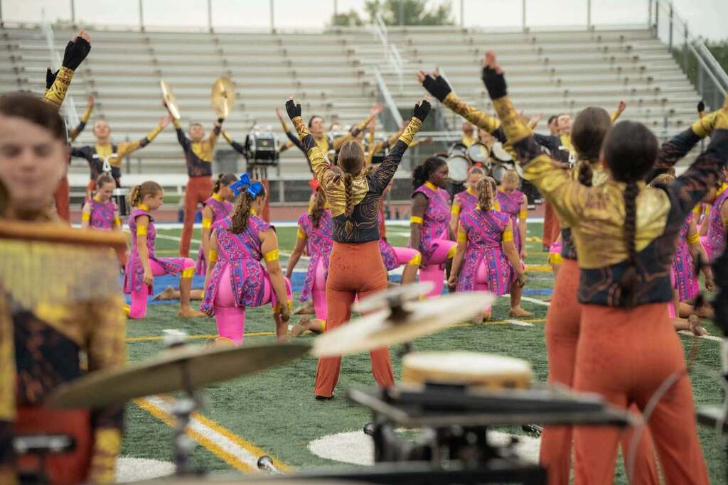 A group of people in matching purple and gold uniforms performing on a football field with musical instruments.