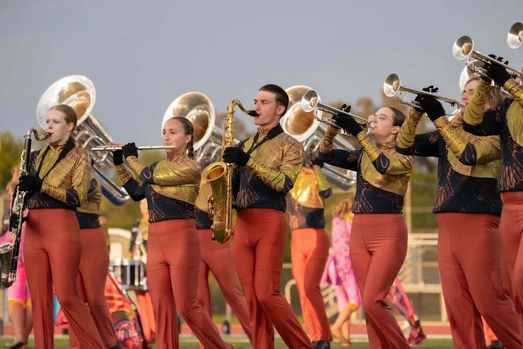 A marching band performs on a field, with musicians playing brass and woodwind instruments, dressed in matching uniforms.