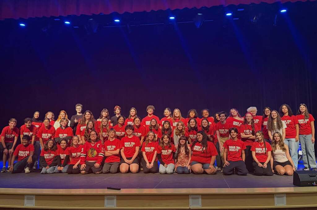 Group in red shirts posing for photo on stage with blue backdrop and blue stage lighting.