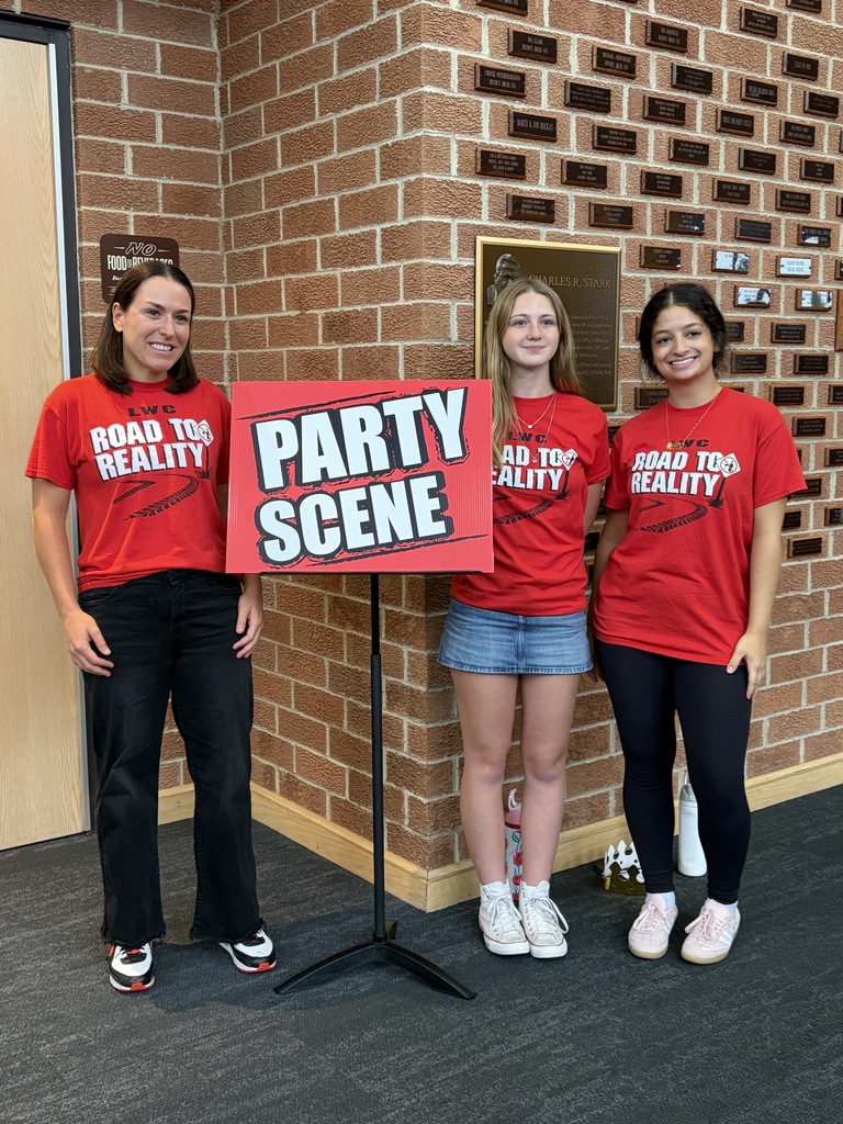 Three people in red shirts stand next to a sign that says "PARTY SCENE". A brick wall is in the background.