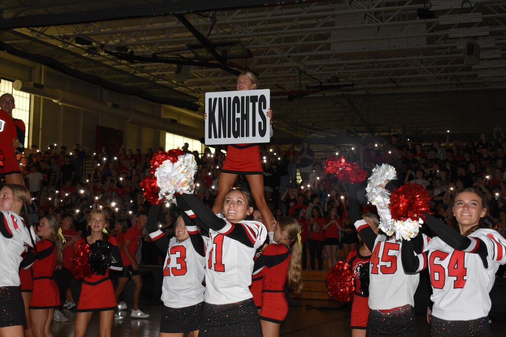 Cheerleaders holding up signs for Knights in a gymnasium, with numbers 13, 1, 15, and 64.