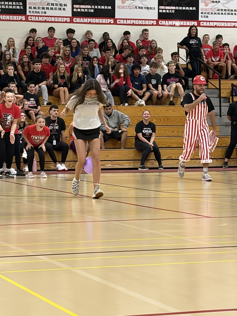 Two people in striped and white outfits perform a jump rope routine in a gym with bleachers full of spectators.