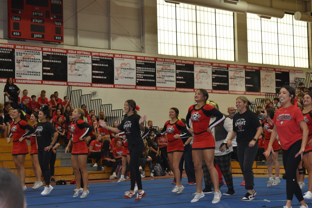 A group of cheerleaders in red and black uniforms performing on a blue mat in a gym.