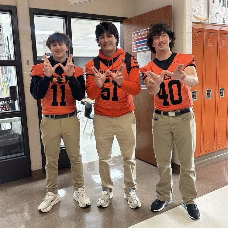 Three young men in orange jerseys with numbers 11, 51, and 40, standing in a hallway.