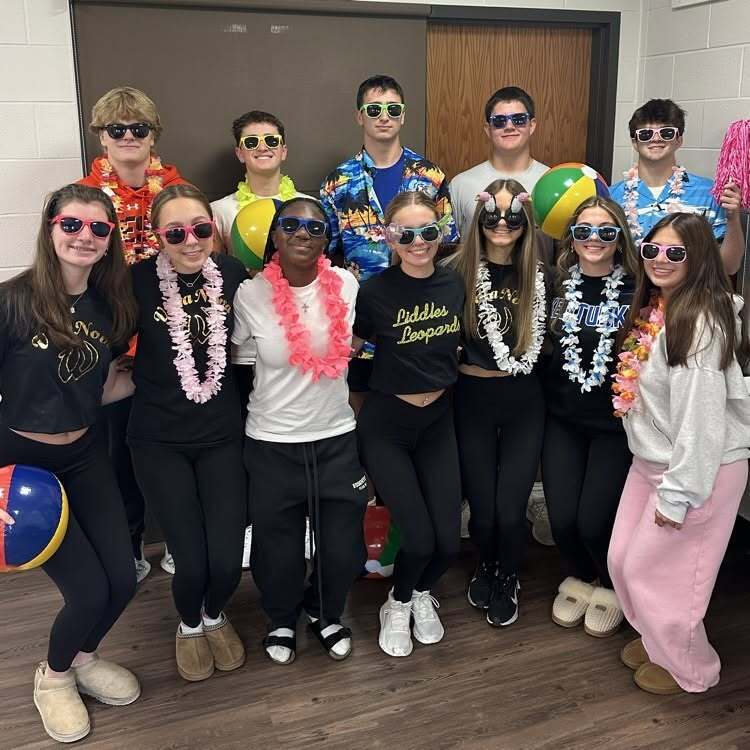 Group of people in matching costumes with sunglasses, leis, and beach balls posing in a room.