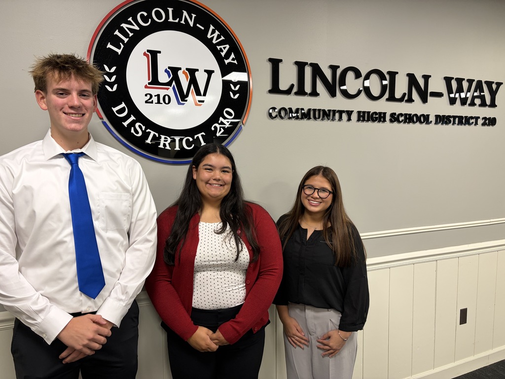 Three students stand together, smiling, in front of a sign with the words "LINCOLN-WAY COMMUNITY HIGH SCHOOL DISTRICT 210."