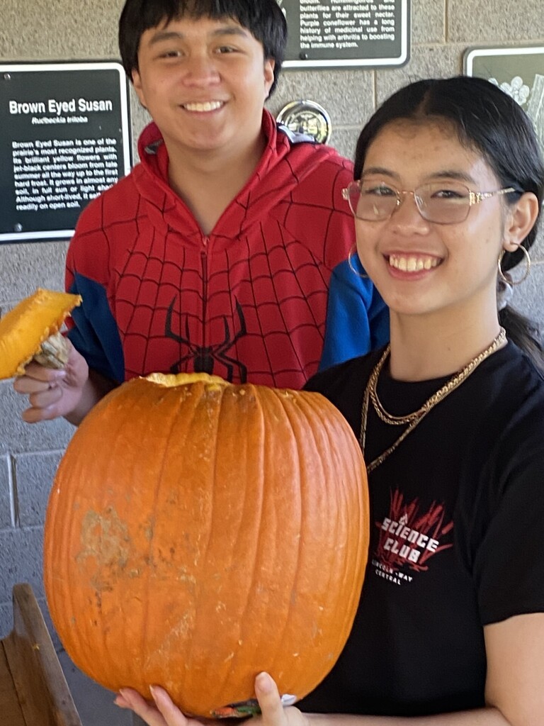 Two students, one in a Spider-Man hoodie, the other in a black shirt, hold a pumpkin.