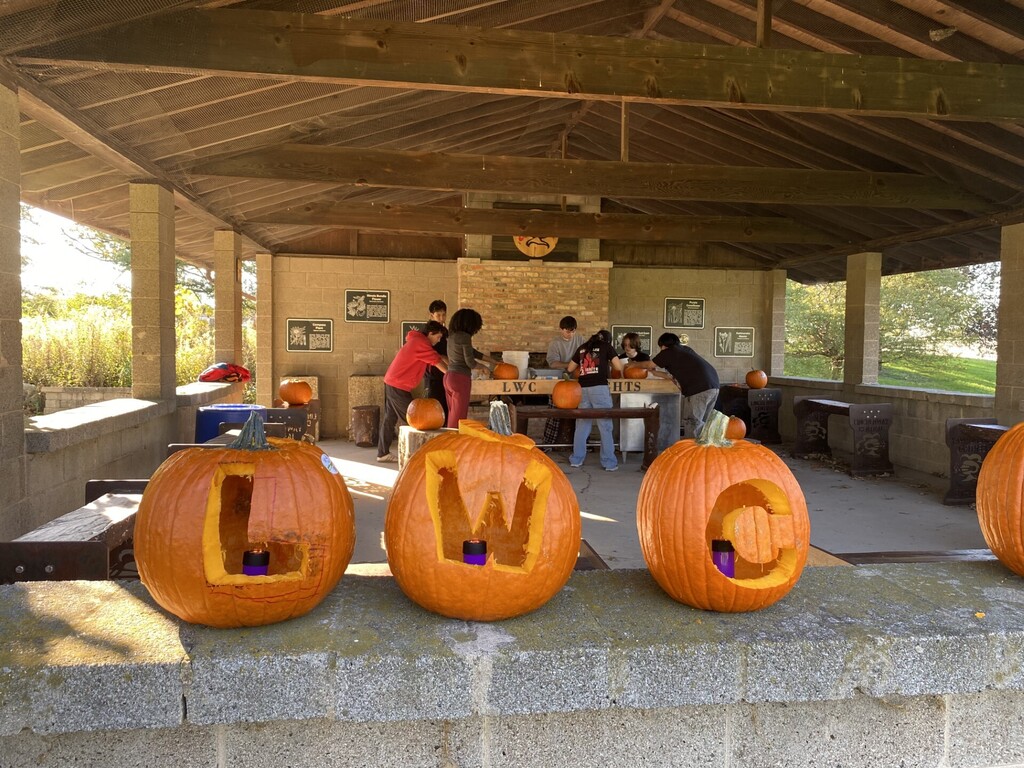 Students carve pumpkins with letters 'LW' and 'C' on them, with three on a ledge.