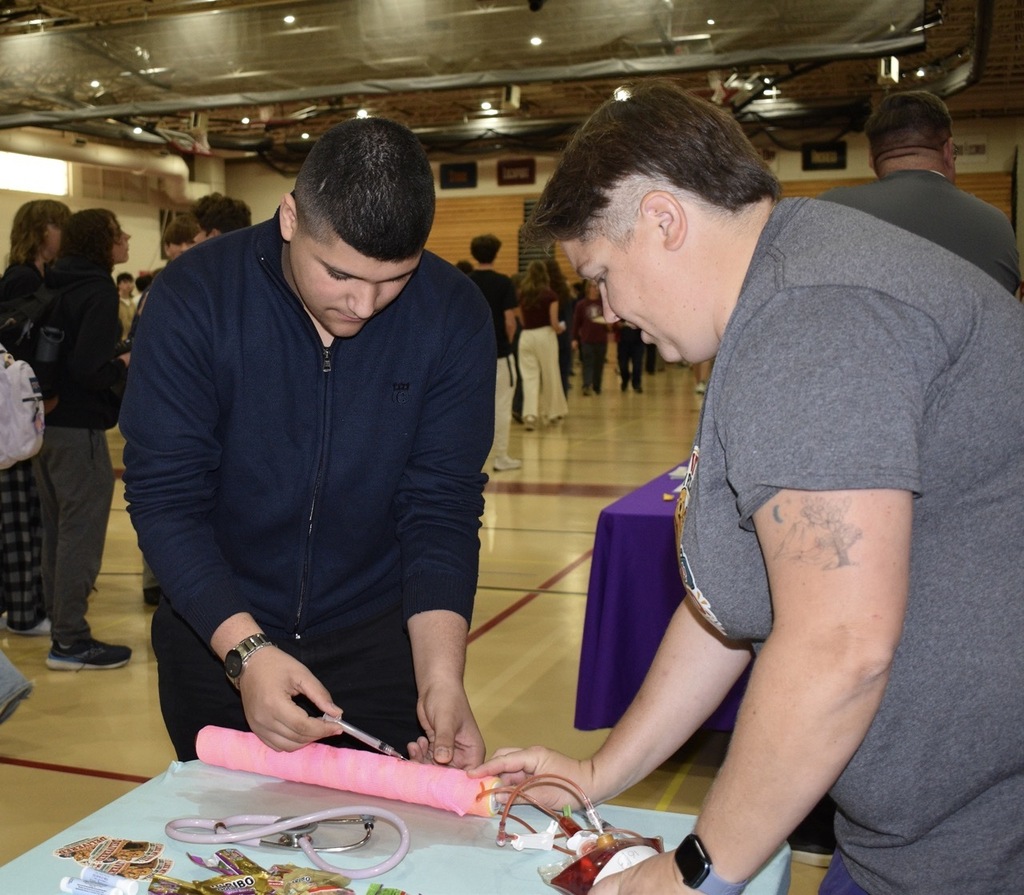 Two individuals working together at a table with objects. One holding a pink object.