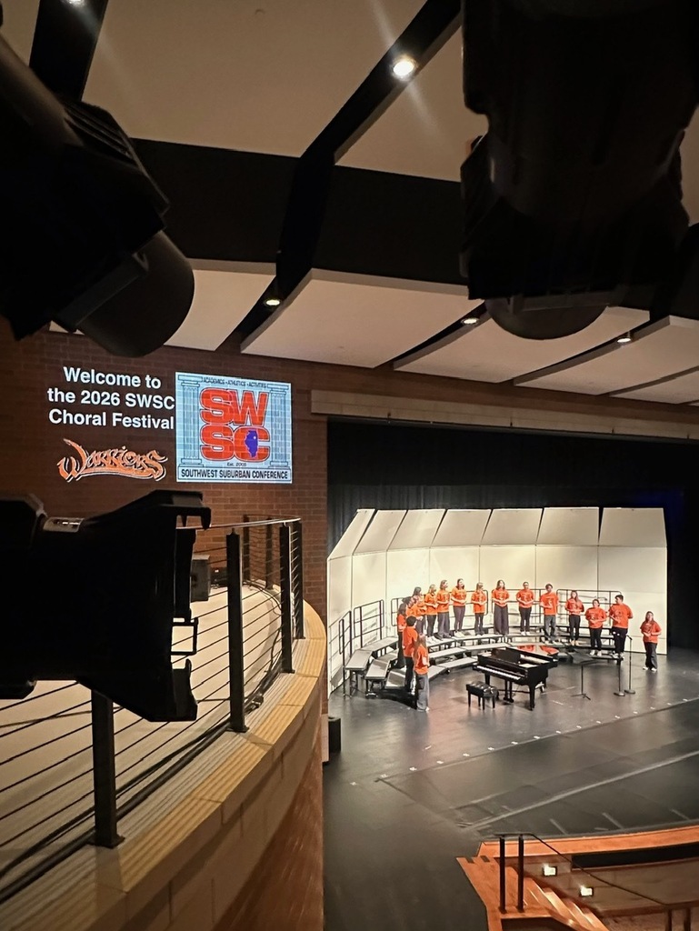 A large room with stage, choir, piano, and projector screen with a message. A balcony overlooks the stage.