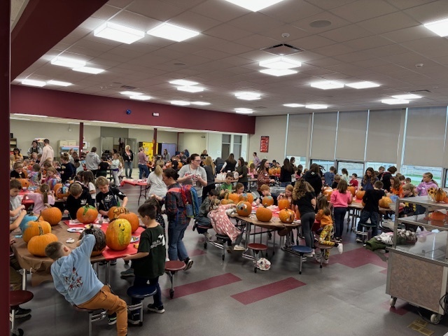 Cafeteria full of tables with children sitting and decorating pumpkins.