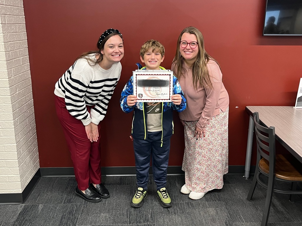 Two smiling female teachers with a smiling boy holding a certificate
