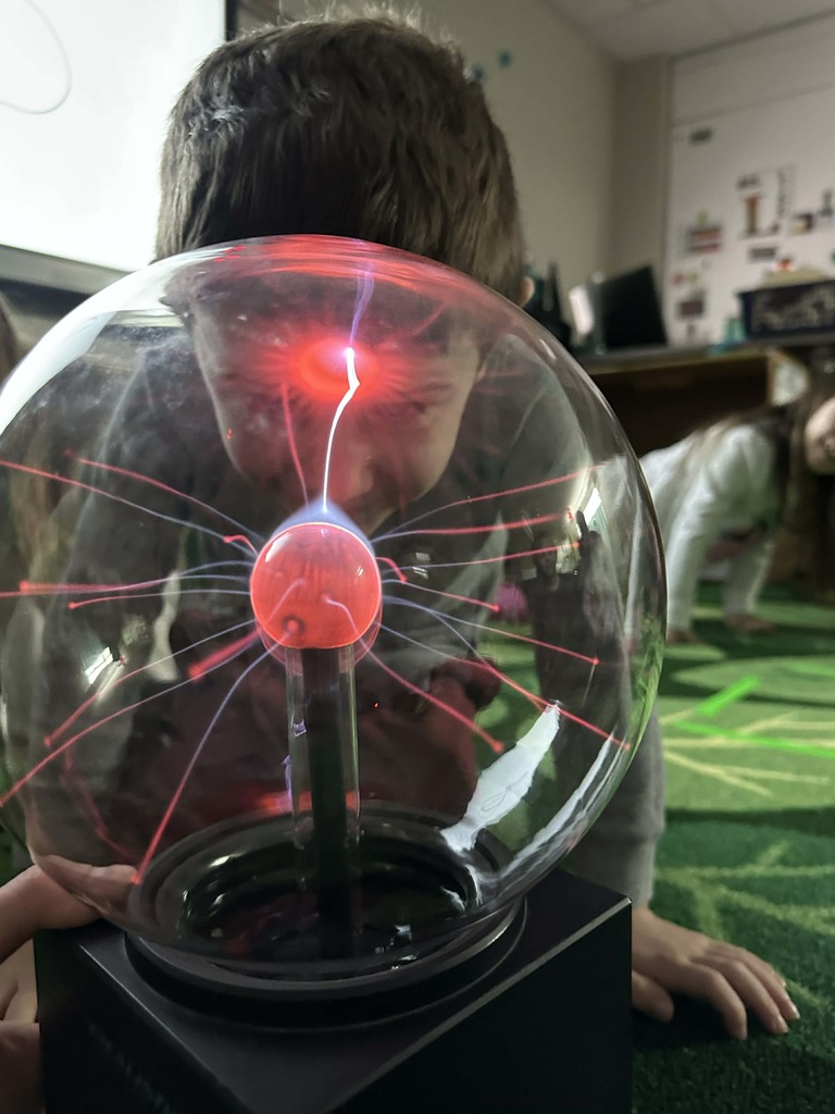 A student observes a plasma globe, with bright pink and purple electrical arcs jumping from the center to where their forehead touches the glass.