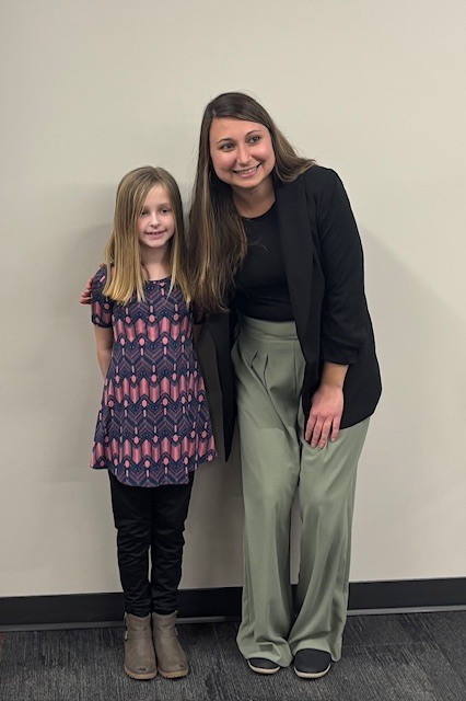 A third grade female teacher is standing next to her female student. Both are smiling after the student was recognized as the teacher's student of the month.