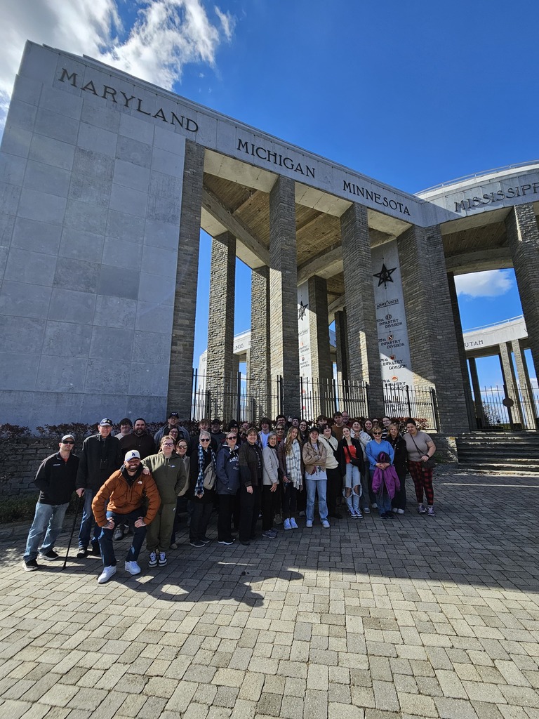 Group of students standing in front of a pillar that says Michigan at the Henri Chapelle Memorial in Belgium