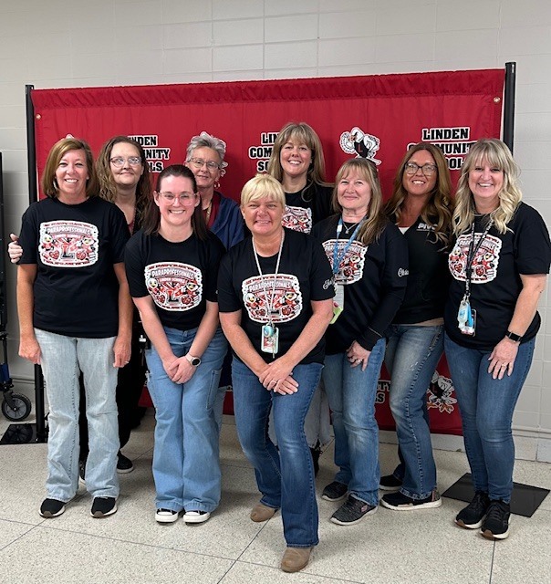 Nine women wearing the same black t-shirts and blue jeans. They are smiling after being recognized for their support and care of children.