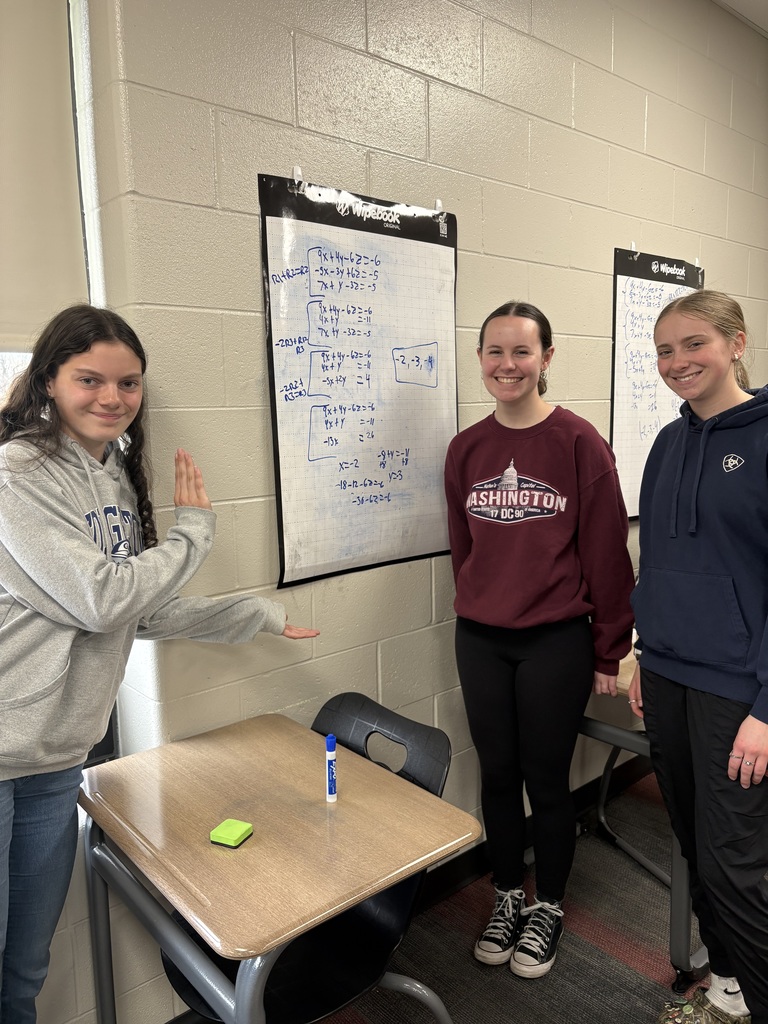 Smiling students displaying their work on vertical white boards
