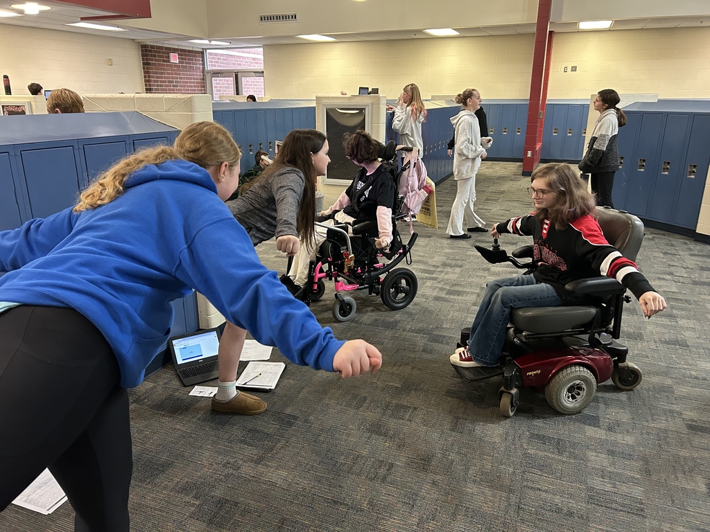 A group of girls practices yoga poses. Two students in wheelchairs do an arms version of the standing yoga poses. 