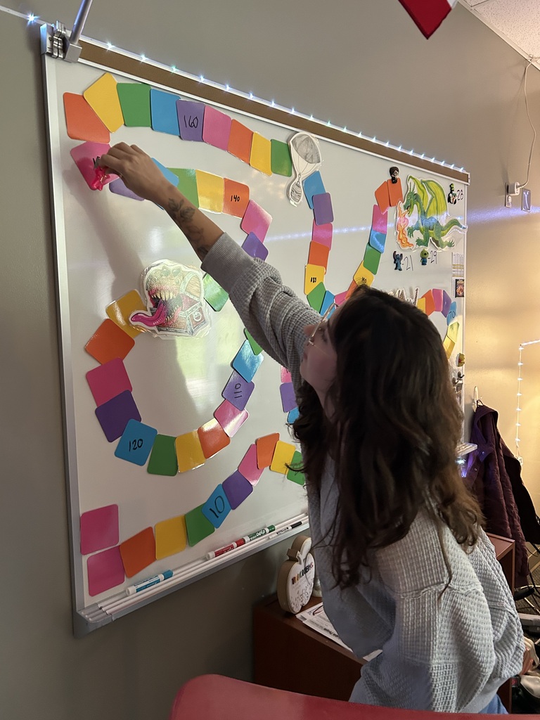The teacher moves a classes game, piece on the game board fixed to a whiteboard