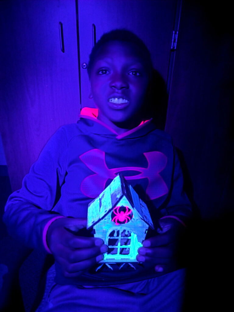 A student holds his spooky, glowing house project.