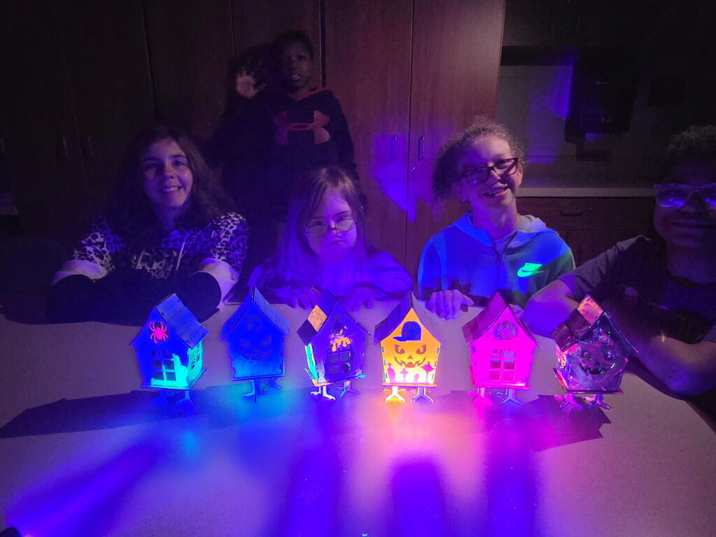 Mrs. Croff’s Class sitting behind their glowing spooky houses under black light.