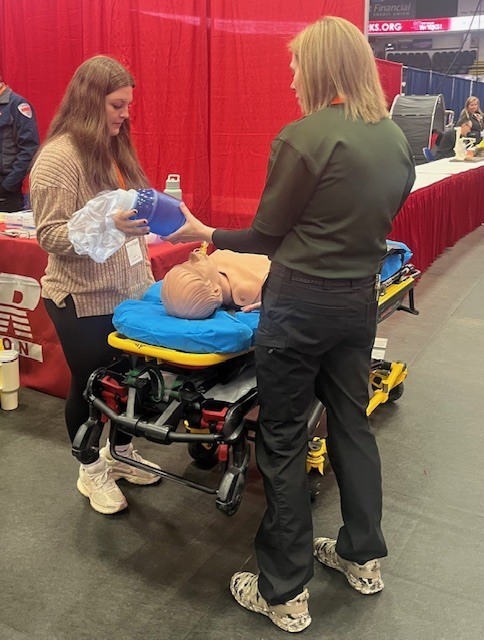 A student practices using a bag valve mask (BVM) medical resuscitator on a medical mannequin on a stretcher 